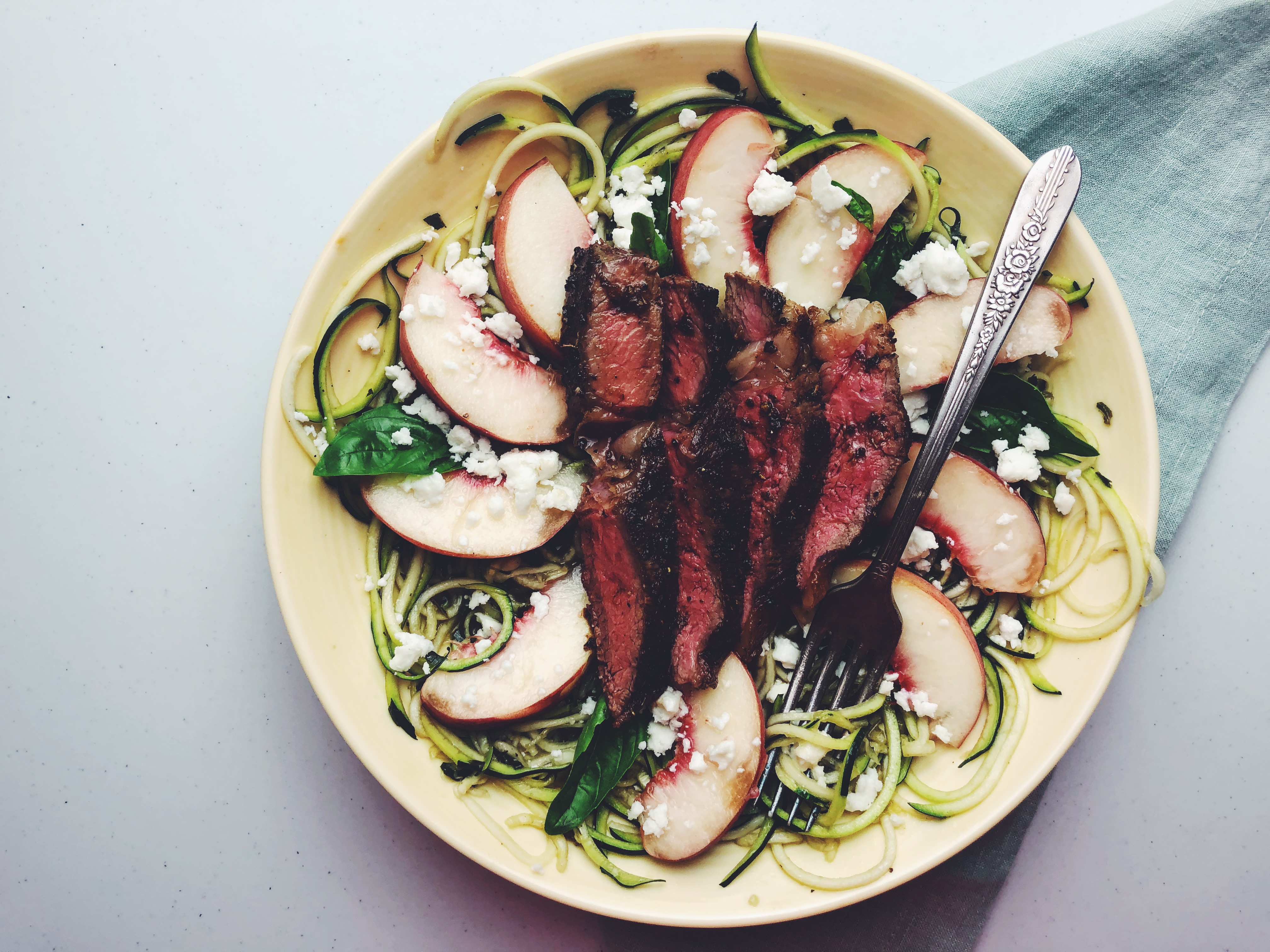 Zucchini Noodle Salad topped with white peaches and sirloin steak.